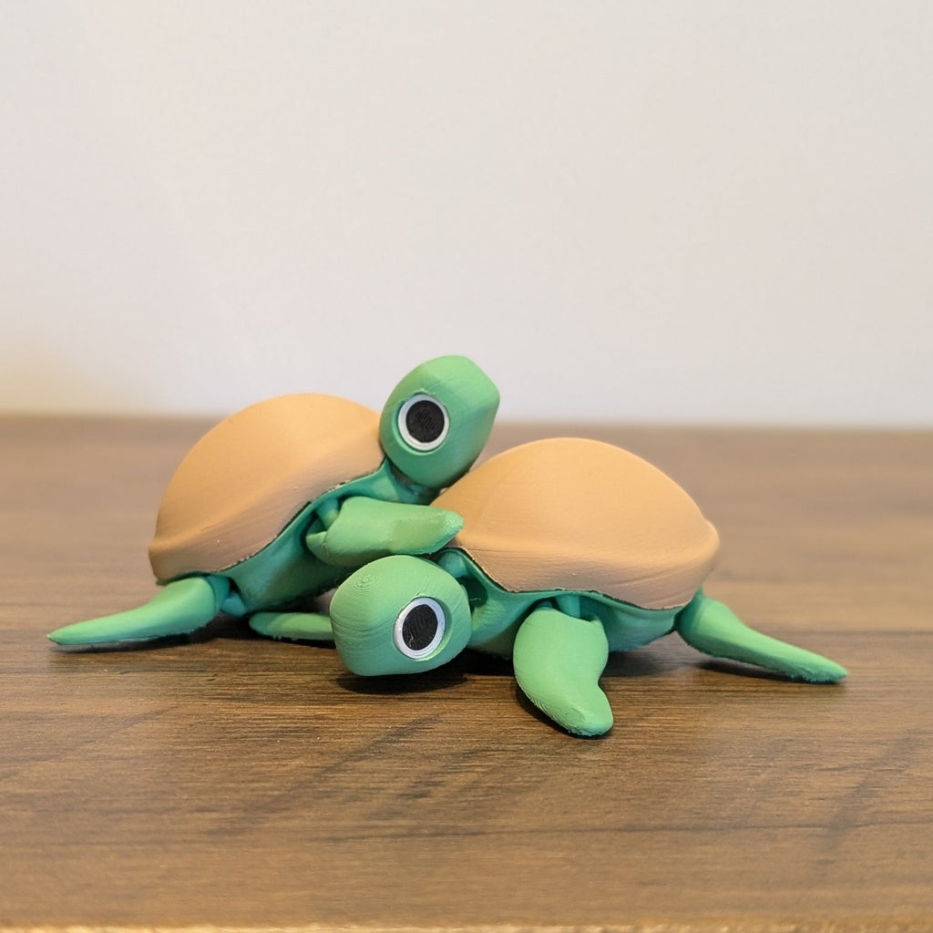 A small decorative figurine of two green sea turtles with tan shells, posed on a wooden tabletop against a plain light wall.