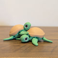 A small decorative figurine of two green sea turtles with tan shells, posed on a wooden tabletop against a plain light wall.